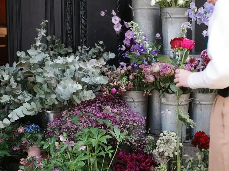 A florist setting a rose into a display of flowers in metal buckets outside her shop